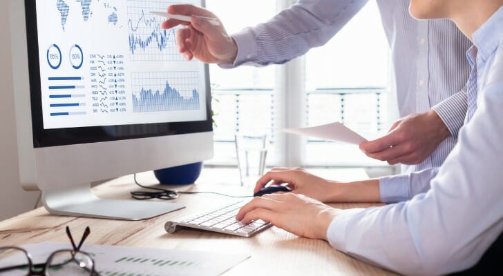 A man using a computer with another man besides him.